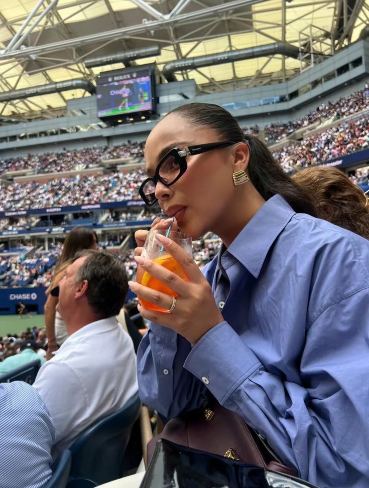 a woman drinking orange juice at a tennis match