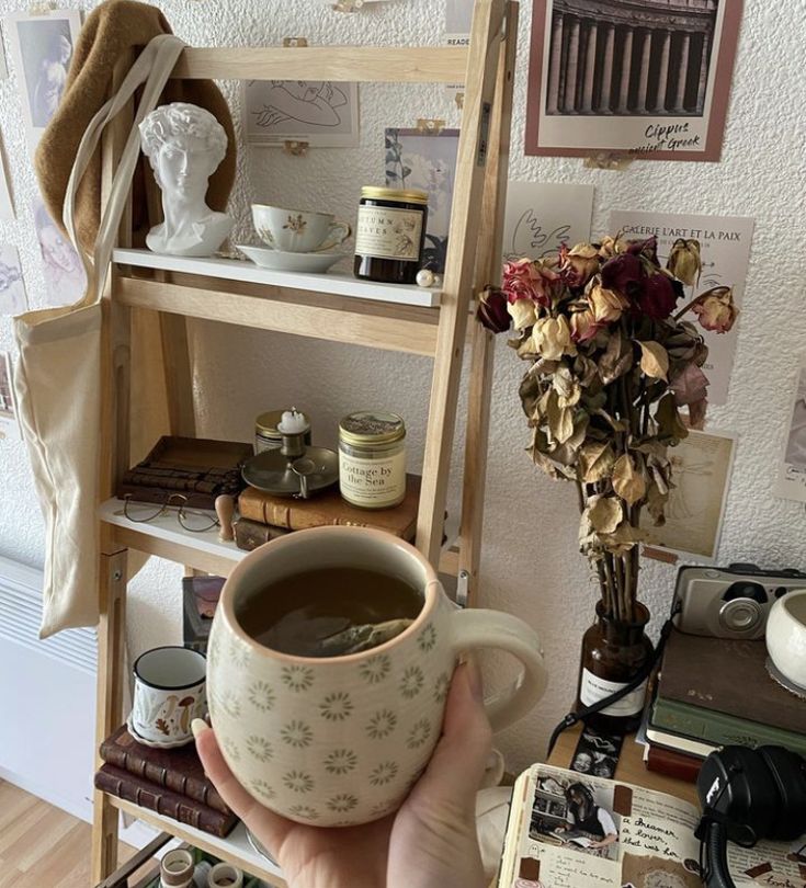 a person holding a cup of coffee in front of a shelf with books and other items