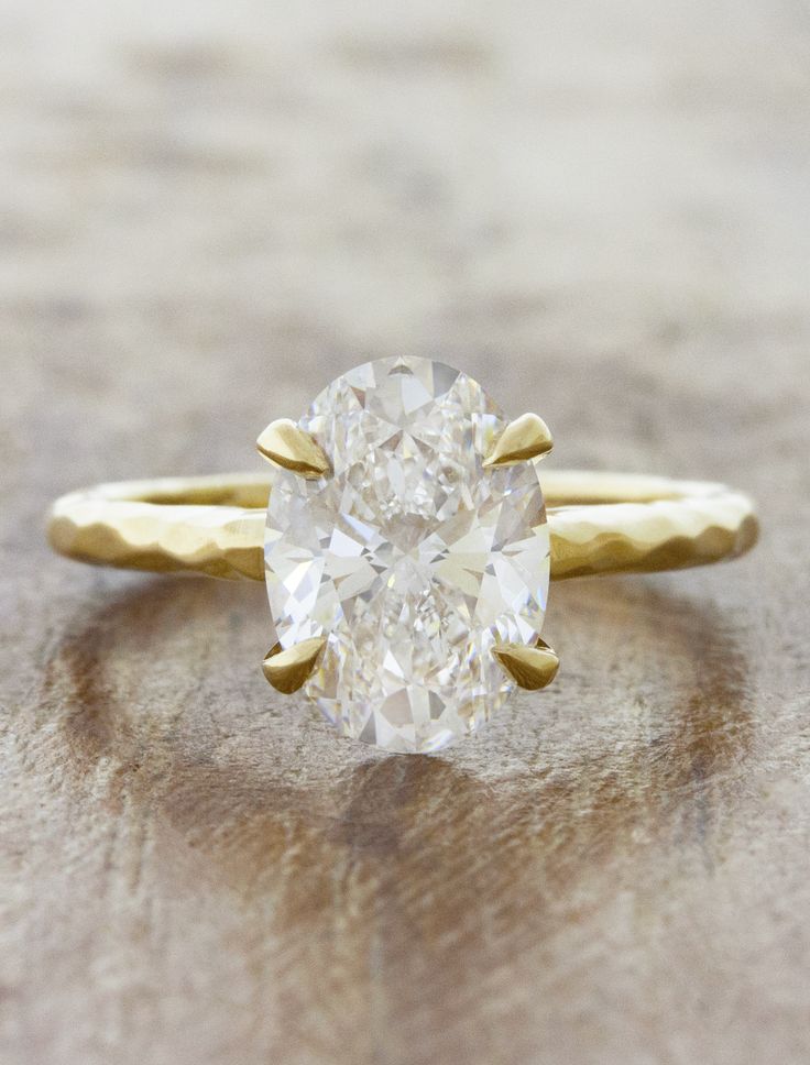 an oval cut diamond sits on top of a gold band and is flanked by two thin bands