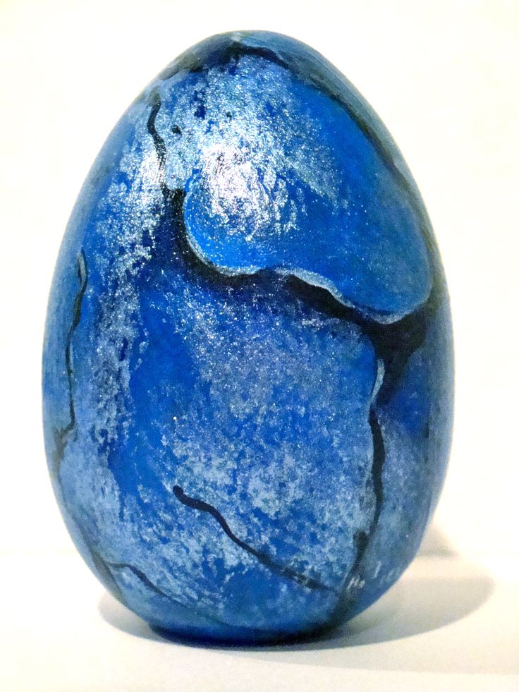 an egg with blue paint on it sitting in front of a white background