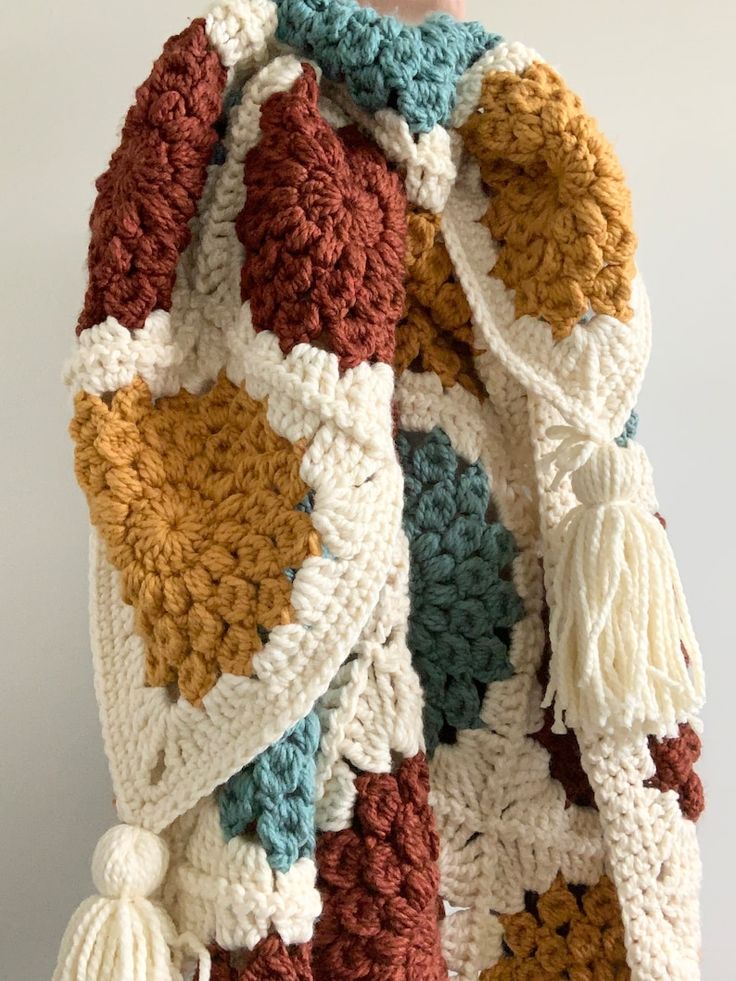 a multicolored crocheted blanket with tassels hanging from the back