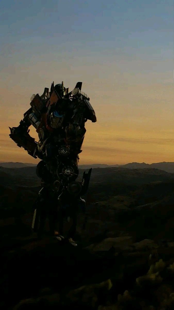 the silhouette of a giant robot standing on top of a hill at sunset with mountains in the background