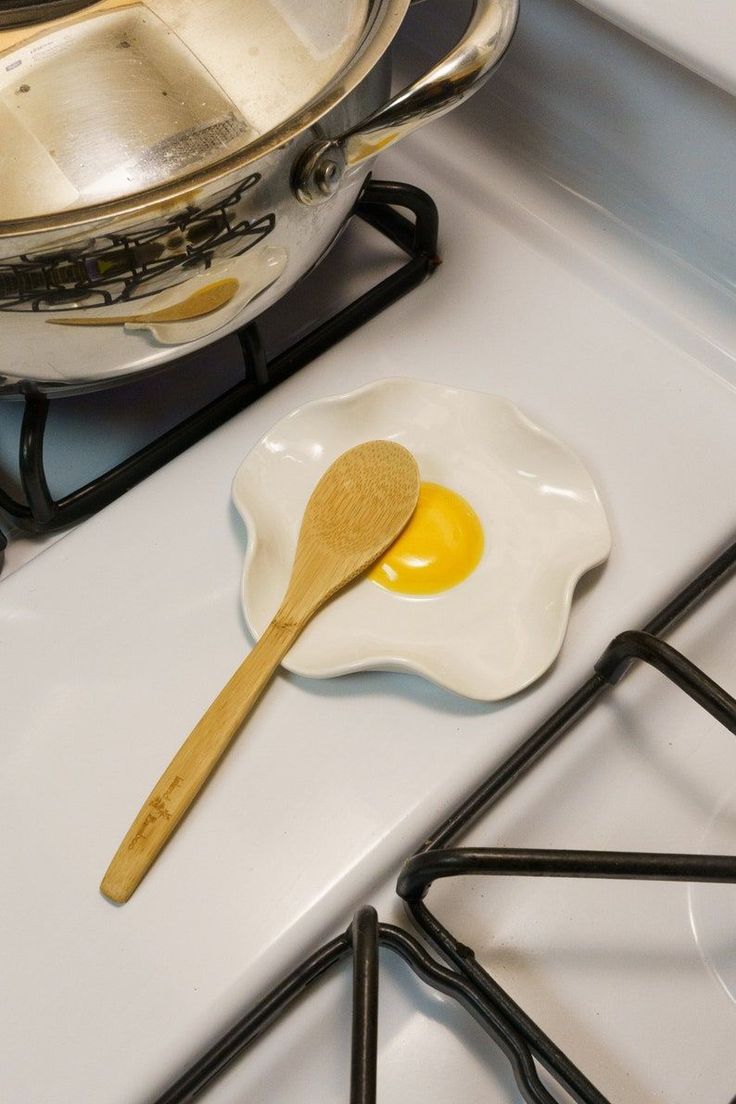 an egg in a frying pan and a wooden spoon sitting on the stove top