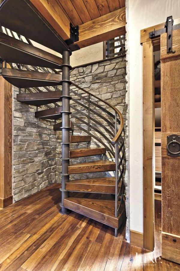 a spiral staircase in the corner of a room with wood floors and stone wall behind it