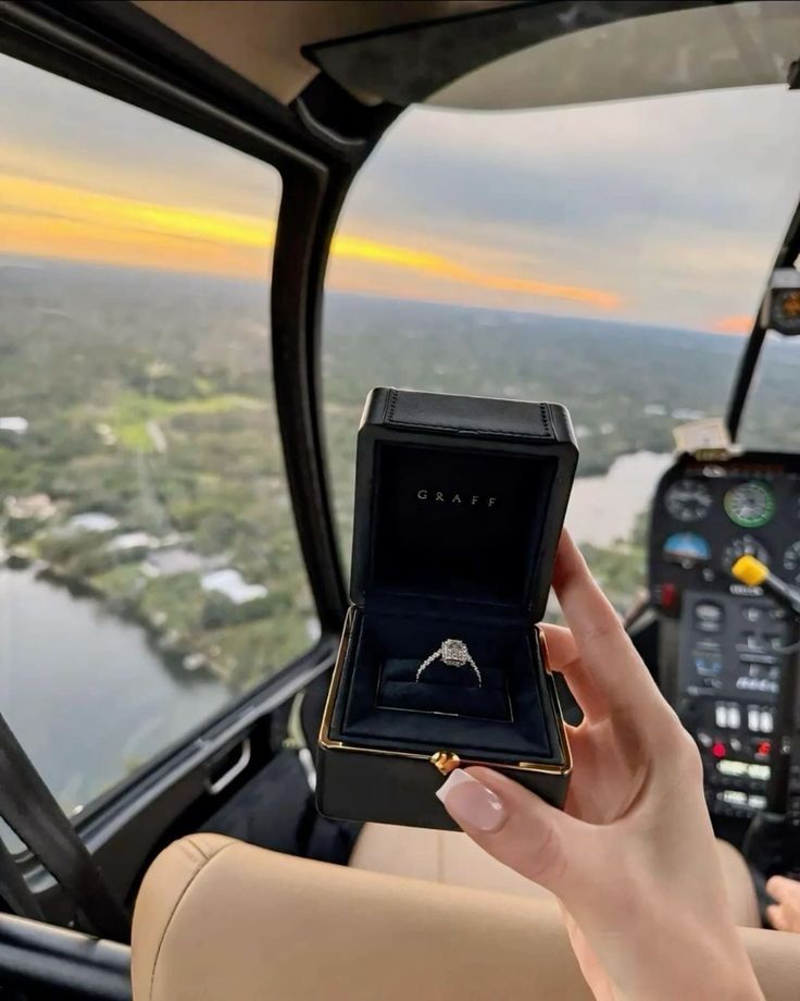 a woman holding up a ring in the cockpit of a plane with an aerial view