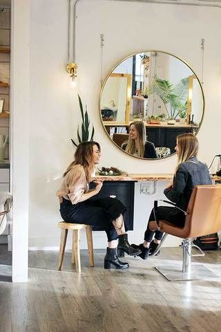 two women sitting at a table in front of a mirror and having their hair done