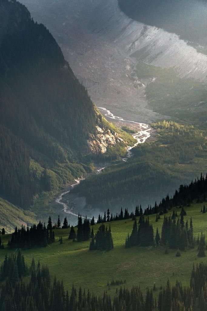 the mountains are covered in green grass and trees, with water running through them on either side