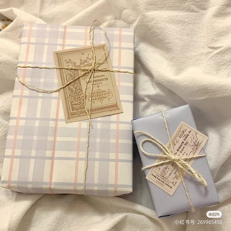 two wrapped gift boxes tied with twine on top of a bed covered in white sheets