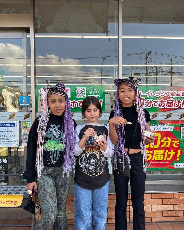 three girls with purple dreadlocks standing in front of a storefront and pointing at the camera