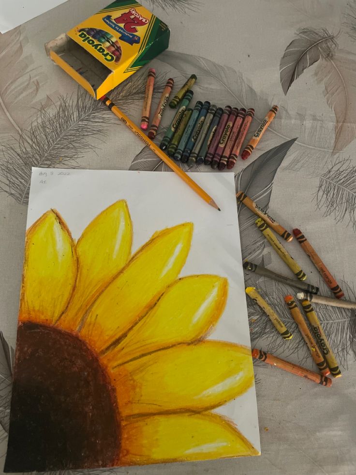 some crayons are laying next to a drawing of a sunflower