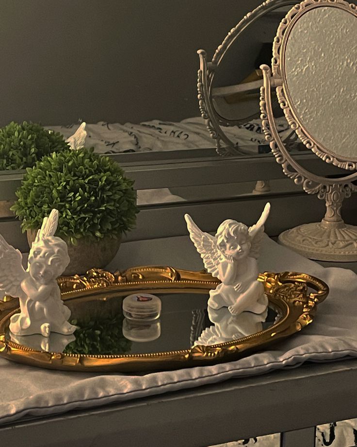 two angel figurines sitting on top of a table next to a mirror and potted plant