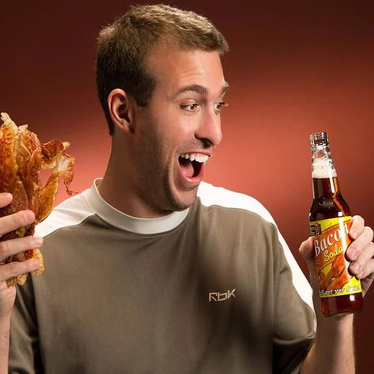 a man holding a beer and food item in his hand while making a funny face