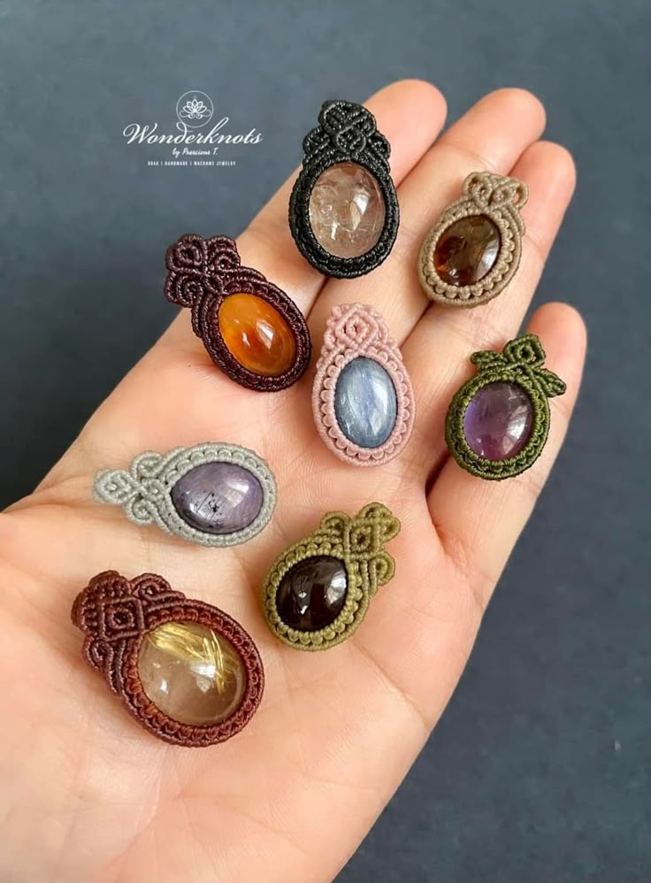 a hand holding six different colored stone rings