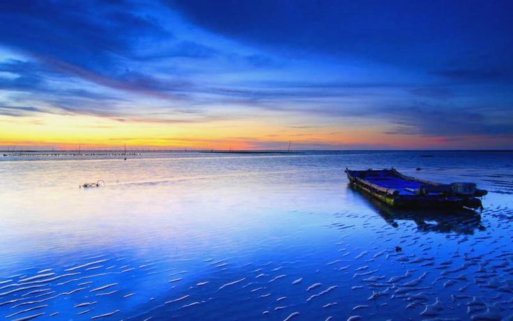 a boat sitting on top of a sandy beach under a cloudy blue sky at sunset