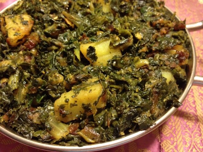 a pan filled with greens and potatoes on top of a pink tablecloth covered table