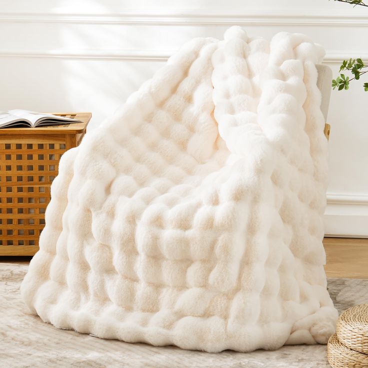 a white blanket sitting on top of a wooden floor next to a basket and plant