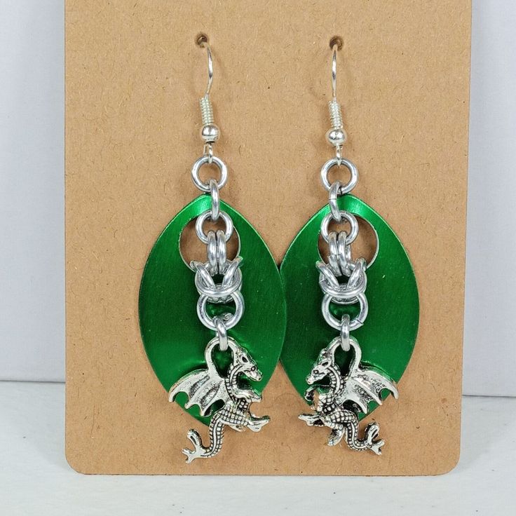 a pair of green and silver earrings with dragon charms on it's earwires