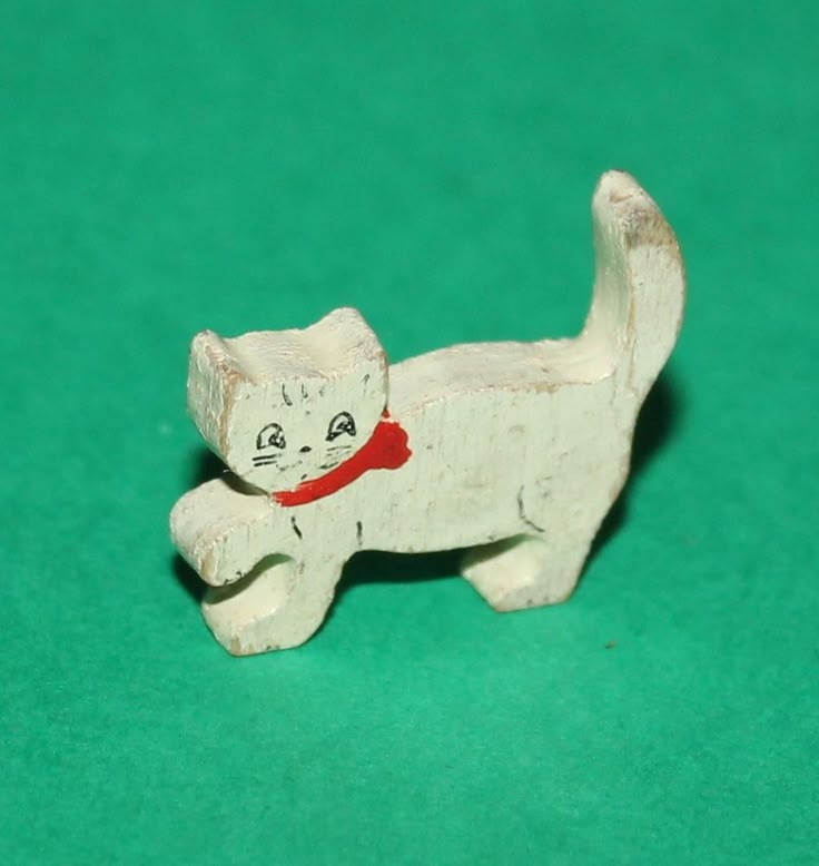 a white cat figurine with a red collar on it's neck sitting on a green surface