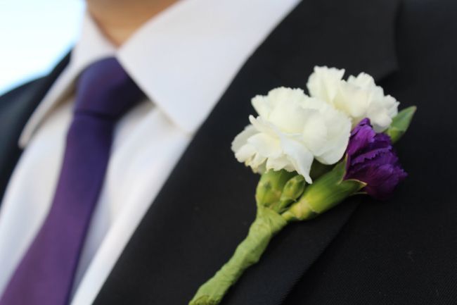 a boutonniere with white and purple flowers attached to the lapel of a man