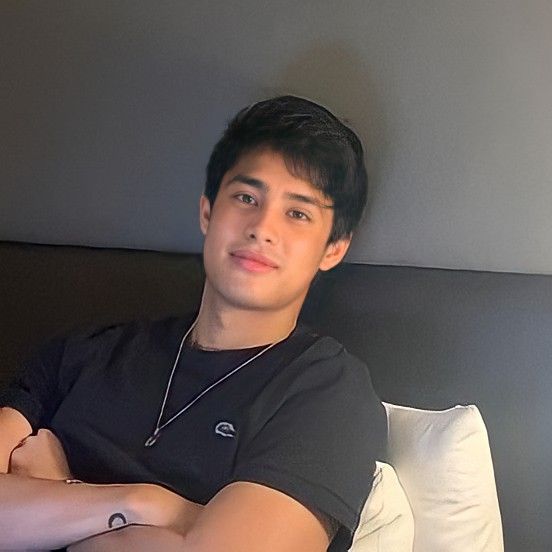 a young man sitting on top of a bed next to a white pillow with his arms crossed