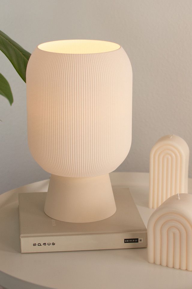 a white lamp sitting on top of a table next to a book and a plant