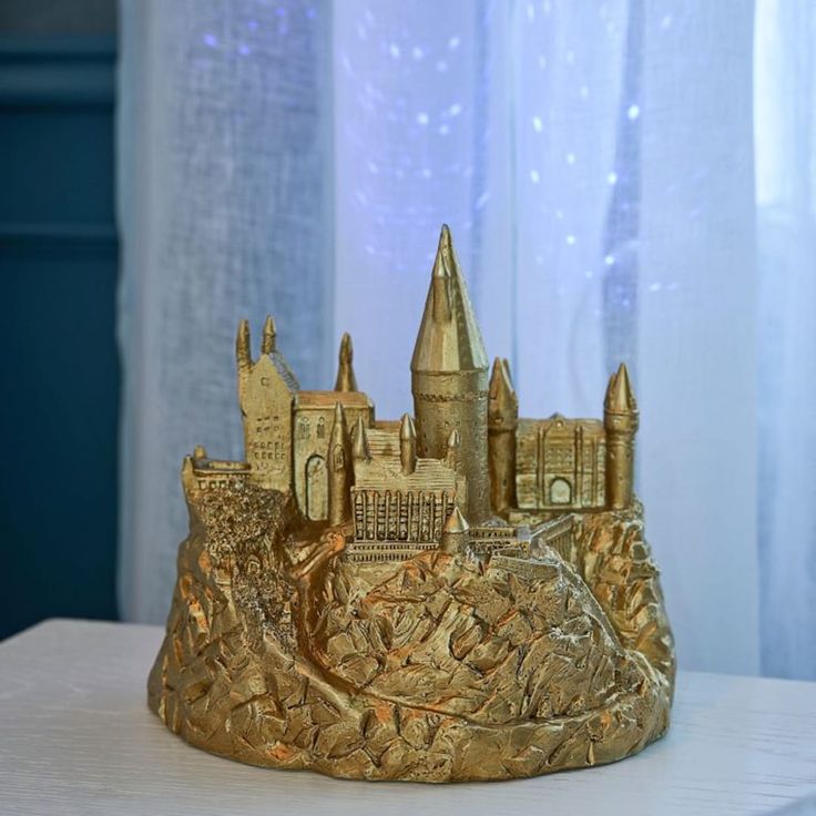 a gold colored castle is sitting on a white table next to a window with sheer curtains