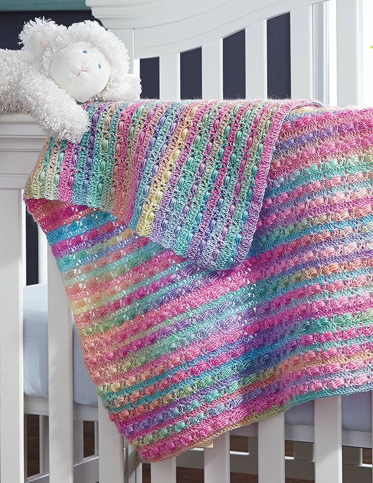 a crocheted blanket draped over a white crib with a teddy bear on it