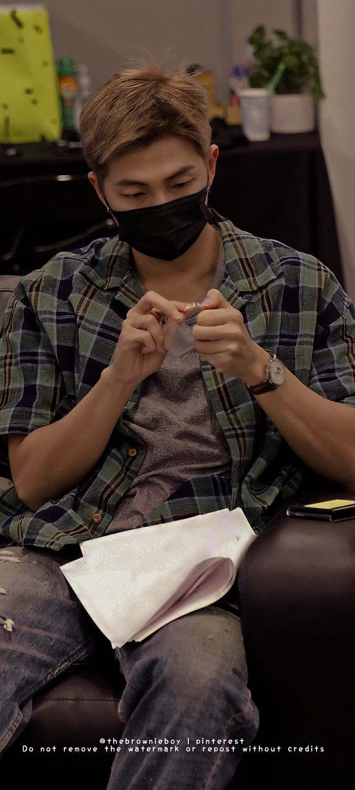 a young man wearing a black face mask while looking at his cell phone in front of him