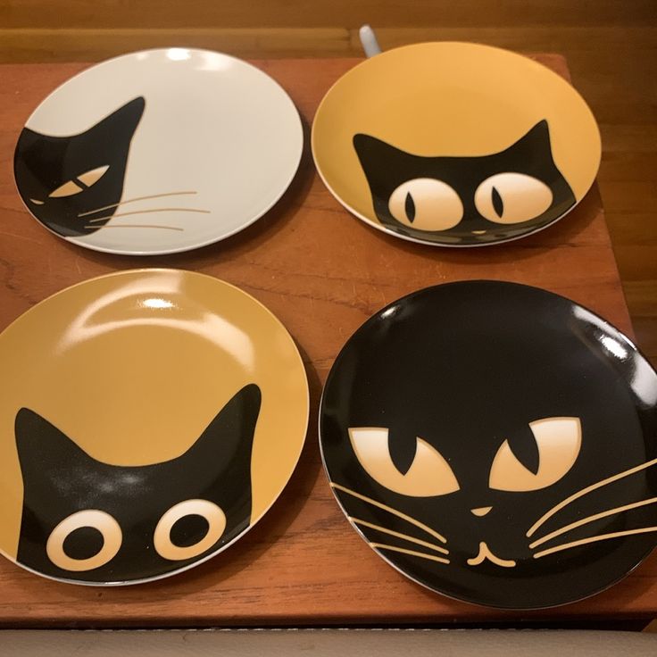 four plates with black cats painted on them sitting on a wooden table next to each other