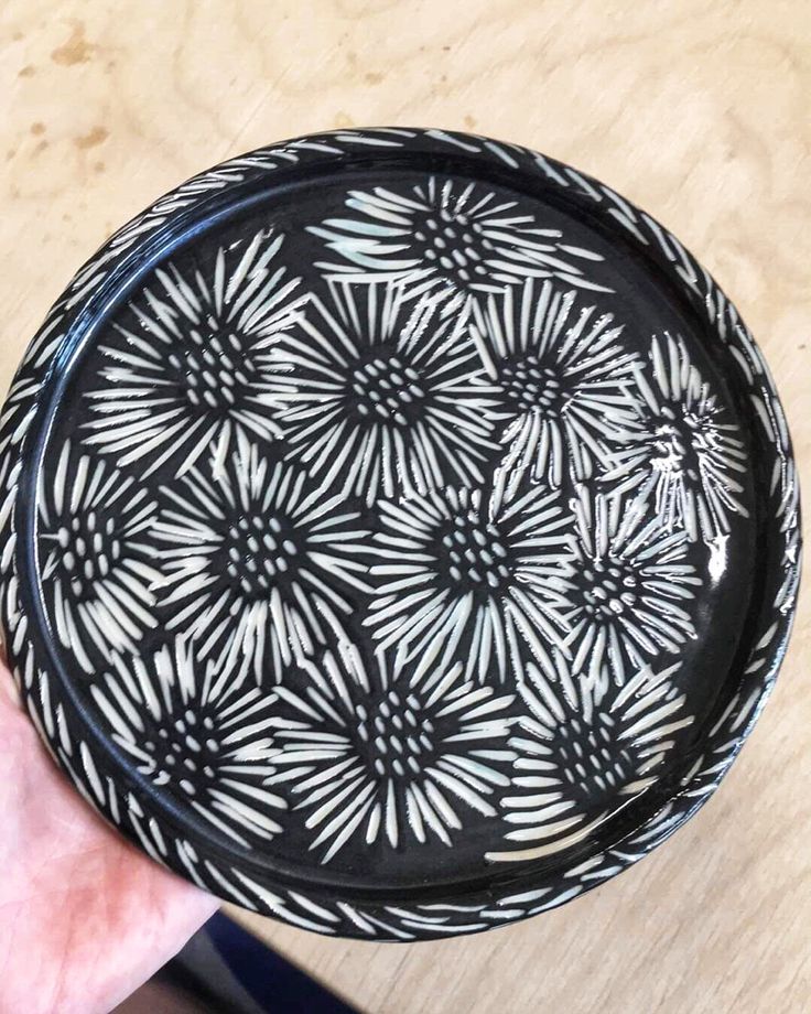 a hand holding a black and white plate on top of a wooden table