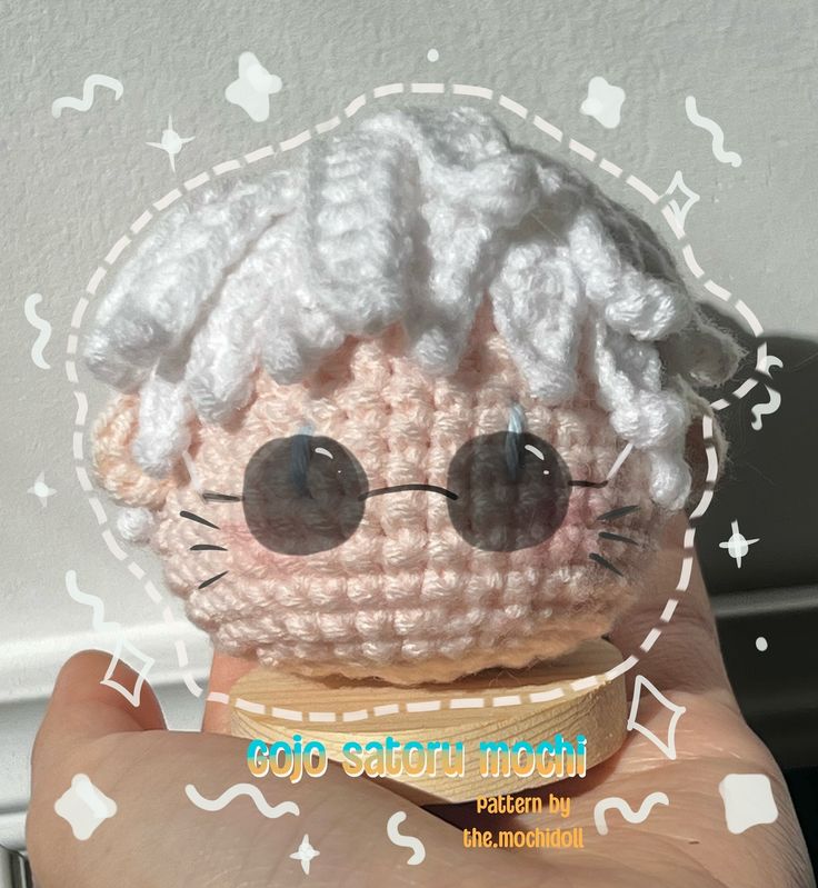 a small crocheted doll with big eyes and white hair is held up to the camera