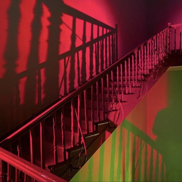 the shadow of a person standing at the top of a stair case in front of a red and green wall