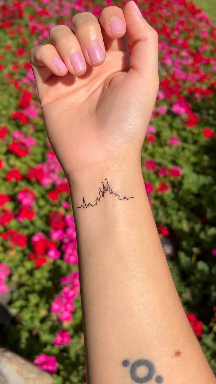 a woman's arm with a small tattoo on it and flowers in the background