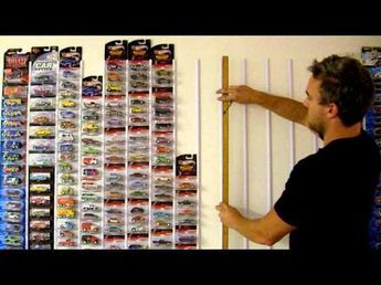 a man is holding a ruler in front of a wall full of hot wheels