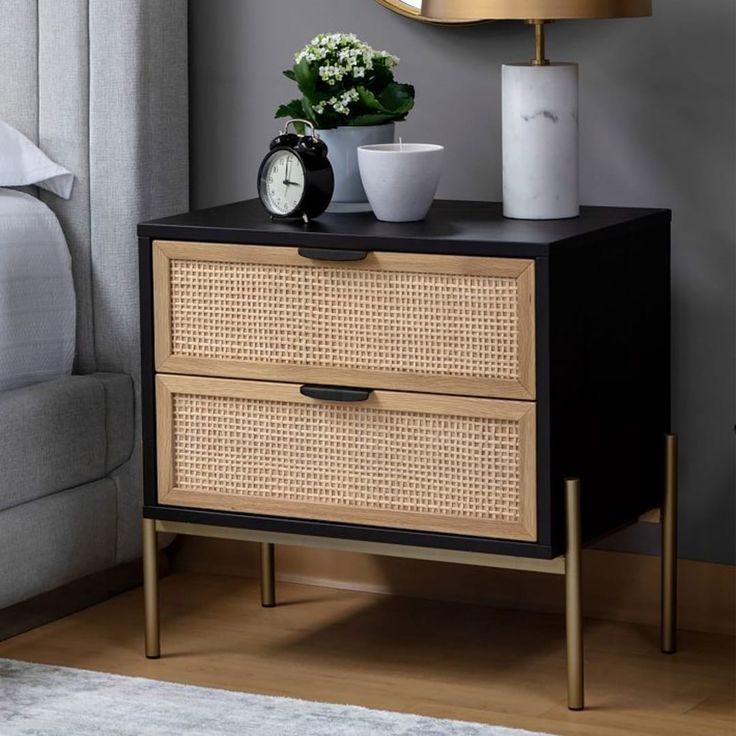 a nightstand with two drawers and a clock on it next to a bed in a bedroom