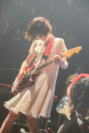 a woman in a white dress is playing an electric guitar on stage with other people