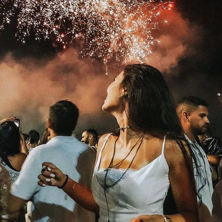 a group of people standing around each other with fireworks in the sky behind them and onlookers watching