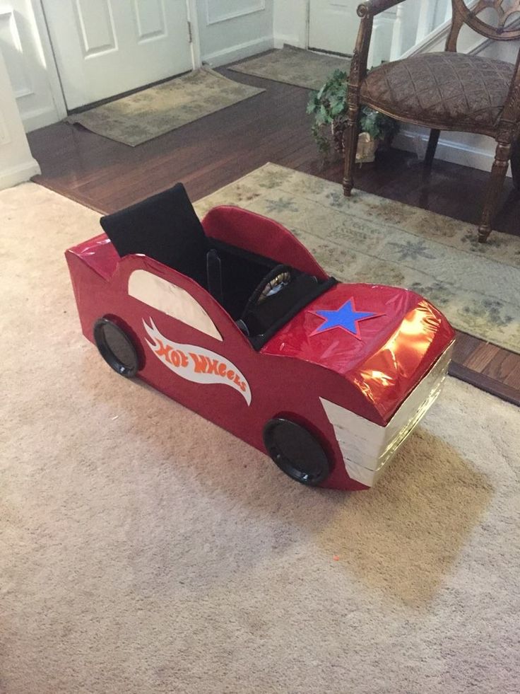 a cardboard race car sitting on the floor in front of a door with a chair behind it