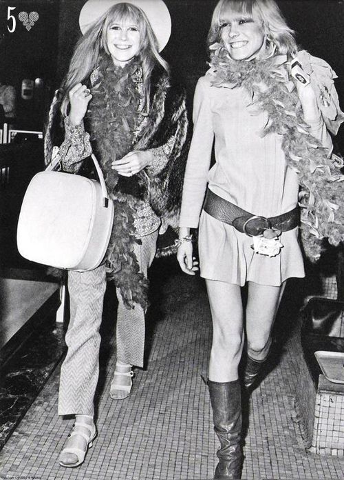 two women dressed in costumes walking down a hallway together, one carrying a bag and the other holding a purse