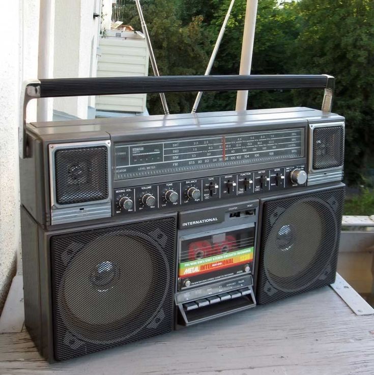 an old fashioned radio sitting on top of a wooden table next to a building and trees