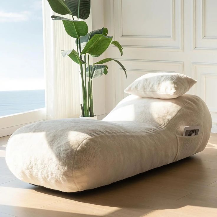 a white bean bag chair sitting on top of a hard wood floor next to a plant