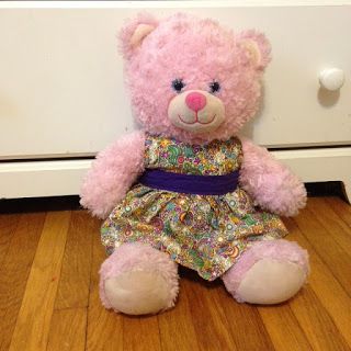 a pink teddy bear sitting on the floor next to a white drawer with drawers in it