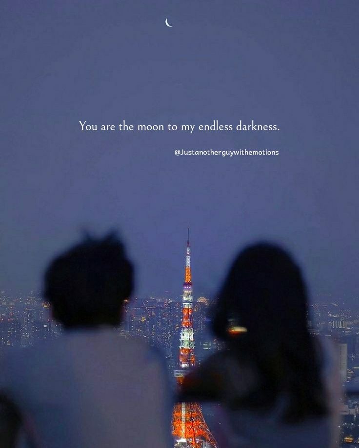 two people sitting on top of a building looking at the city lights and moon in the sky