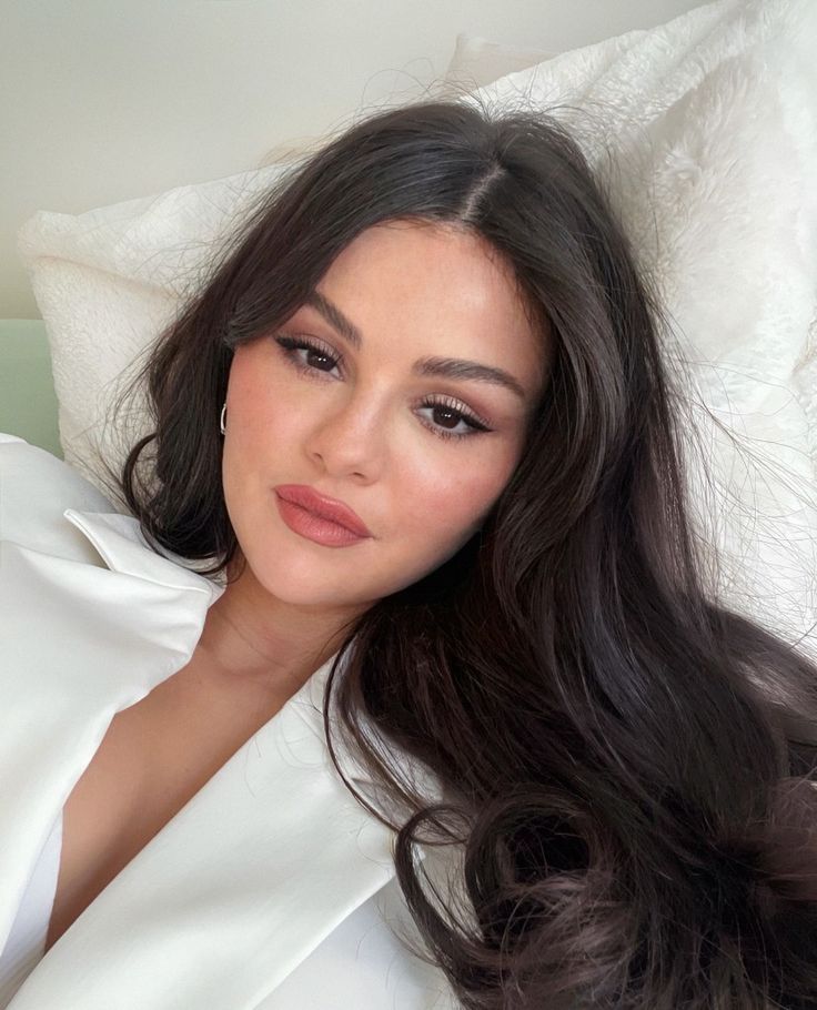 a woman laying on top of a bed next to a white sheet covered pillow with her hair blowing in the wind