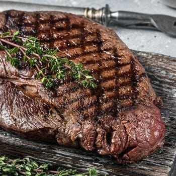 a piece of steak on a wooden cutting board next to a knife and some herbs