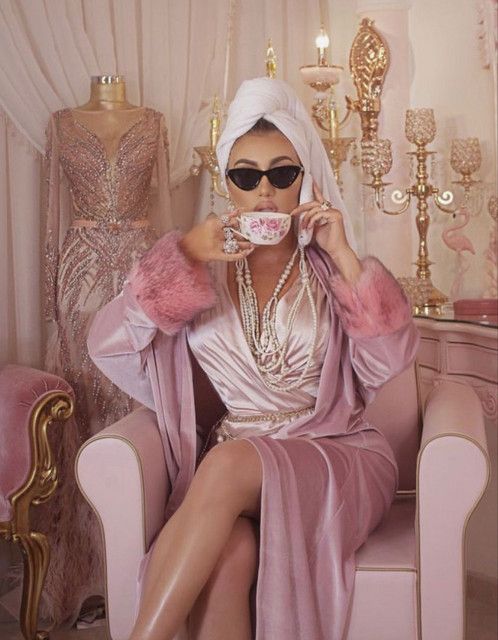 a woman sitting in a chair drinking from a tea cup with her legs crossed and wearing sunglasses