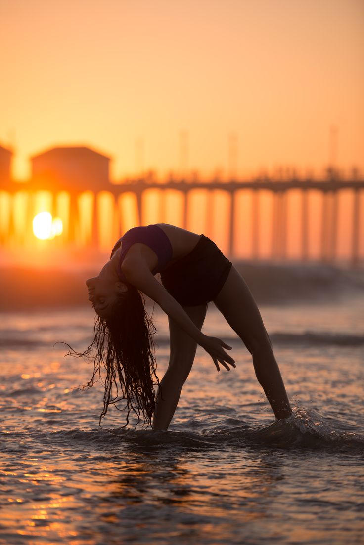 a woman standing in the ocean at sunset with her hands on her hips and head down