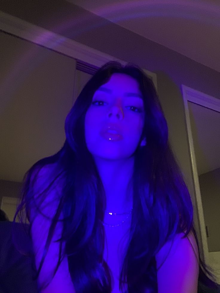 a woman with long dark hair and blue light in her face is looking at the camera