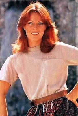 a woman with red hair wearing a white t - shirt and patterned skirt posing for a photo