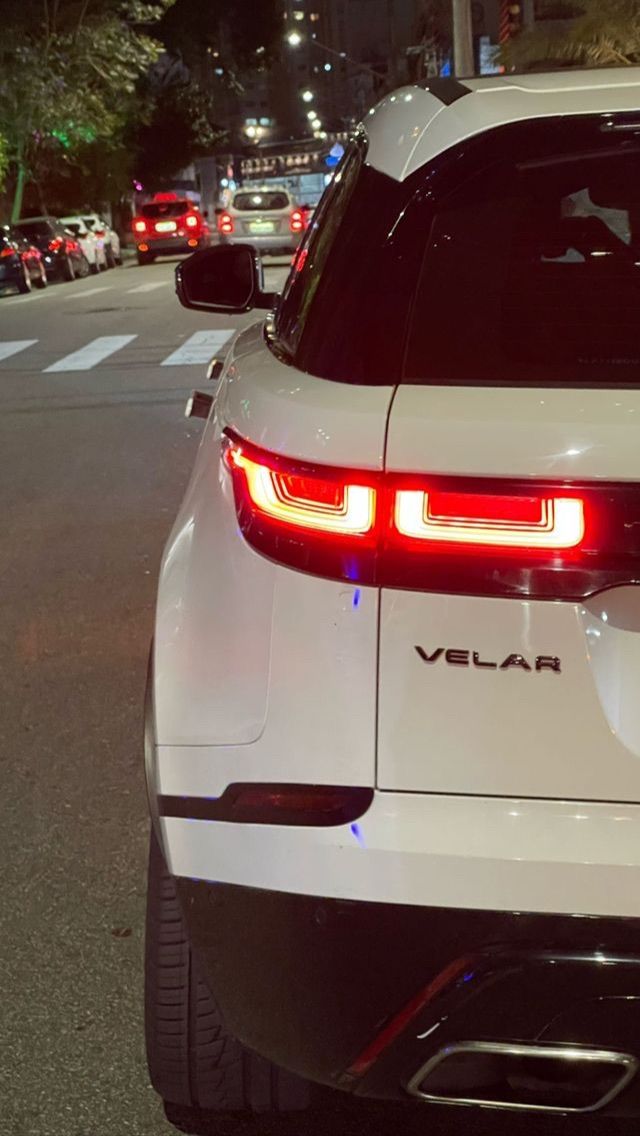 the rear end of a white car parked in front of a street with cars on it